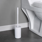 White toilet brush in a matching white holder placed on a gray tile floor next to a white toilet and baseboard.