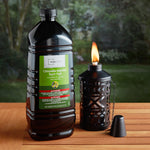 Lifestyle image of Mainstays citronella torch fuel jug beside a lit tabletop torch on a wood surface outdoors.