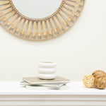 White bubble planter styled on books beneath a round decorative wall mirror and rattan balls