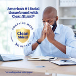 Man at a desk blowing his nose with a tissue, overlaid by a 'Clean Shield contains mess 3X better' emblem