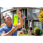 Man attaching a neon-yellow RESCUE! yellowjacket trap to a tree branch with a house and people gardening in background.