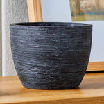 Matte black textured ceramic planter placed on a wooden surface next to framed art