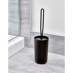 Matte black toilet brush and holder placed on a gray tiled bathroom floor next to a shower curb