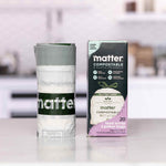 Matter compostable box next to a standing roll of branded bags on a kitchen counter in soft focus