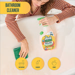 Person wiping a bathtub with a cloth while a Mean Green refillable bathroom cleaner bottle sits on the tub edge.