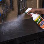 Hand spraying Mean Green Super Strength cleaner from a trigger bottle producing fine mist over a black workbench