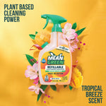 Mean Green refillable bathroom cleaner bottle staged with tropical flowers and mango slices on a bright yellow background.