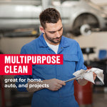 Mechanic in blue coveralls wiping a metal tool with a white STP wipe in a garage setting, promotional multipurpose clean overlay