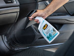 Hand holding and spraying Meguiar's Carpet & Cloth Re-Fresher inside a vehicle, mist visible toward door panel