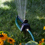 Close-up of Melnor oscillating sprinkler wet on grass with water jets and a garden hose connected