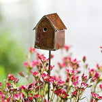 Antique-style metal birdhouse on a stake displayed among small pink flowers in a garden setting