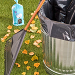 Outdoor scene with metal trash can lined with a black bag, rake, fallen leaves and a wrapped roll of Great Value outdoor trash bags in background