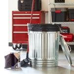 Lifestyle photo showing a metal trash can lined with a black drawstring bag, the product box and broom nearby in a garage setting.