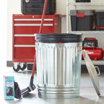 Metal trash can with a black drawstring bag inside and a Great Value trash bag box and broom beside it in a garage setting