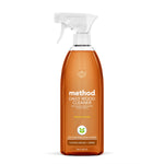 Clear amber spray bottle of Method Daily Wood Cleaner with white trigger and almond labeling on a white background