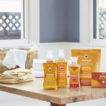 Lifestyle scene on a wooden table showing Method ginger mango detergent and other Method laundry products near folded towels.