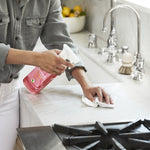 Lifestyle photo of a person using a pink Method spray bottle to clean a marble countertop by a sink