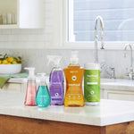 Kitchen countertop scene showing a range of Method cleaning products including a purple all-purpose spray bottle among other bottles and wipes.