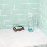 Method Daily Shower spray bottle placed on a marble countertop against pale green subway tile next to a soap dish