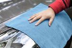 Hand pressing a light blue microfiber cloth against a car headlight while drying or cleaning the surface.
