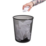 Black metal mesh trash can with hand dropping crumpled paper into it against white background