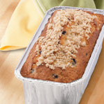 Baked mini loaf with crumb topping presented inside an aluminum foil mini loaf pan on a wooden surface