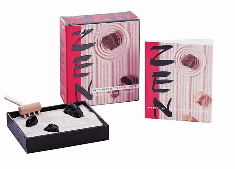 Mini tabletop Zen garden with a black tray of raked sand, three dark stones, a wooden rake, and matching box and booklet