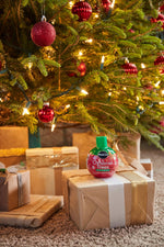 Miracle-Gro Christmas Trees bottle sitting on a wrapped gift beneath a decorated and lit Christmas tree.