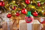 Miracle-Gro for Christmas Trees bottle centered on a wrapped present with ornaments and lights on the tree behind.
