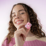 Young person smiling while holding the small pink cow-themed Squishmallows travel cap accessory near their face.