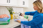 Person spraying Molly's Suds stain remover onto a garment at a kitchen counter with folded towels nearby