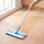 Mop with a disposable wet mopping cloth attached being used on a light wood floor near a window