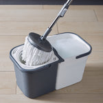 Round mop head being spun in the bucket’s wringer next to a soapy white water compartment on wood floor