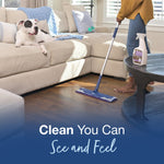 Lifestyle image of a person mopping hardwood floors while a dog watches on the couch and a Bona Pet System bottle sits on the table.