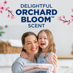 Smiling woman and child holding folded laundry beneath text advertising delightful Orchard Bloom scent with floral accents