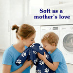 Mother and child smelling a paw-print patterned blanket in a laundry room with headline 'Soft as a mother's love'
