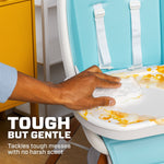 Hand scrubbing food-stained highchair tray with a white Mr. Clean Magic Eraser, text 'Tough but gentle' visible