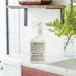Lifestyle image of Mrs. Meyer’s Vinegar Gel spray bottle placed on a bathroom counter with greenery and shelf in background