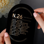 Close-up of black card reading N.26 with descriptive marketing copy held by manicured hands and a flower at left