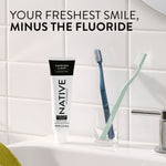 Native Charcoal & Mint toothpaste tube on a bathroom sink with two toothbrushes and tiled wall, overlaid text reading “Your freshest smile, minus the fluoride.”