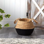 Nearly Natural natural jute basket with black base placed indoors on floor beside rustic barn-style door and greenery
