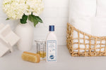 Noodle & Boo laundry detergent bottle in a laundry styling with towels, basket, brush and flowers