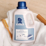 Noodle & Boo baby laundry detergent bottle on a towel with wooden brush, blue striped label and cap