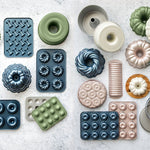 Assorted Nordic Ware bundt and specialty cake pans arranged flat on a light surface, showing various shapes and finishes