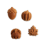 Four baked autumn-shaped cakelets - acorn, pumpkin, pinecone and maple leaf - on a white background