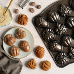 Overhead view of Nordic Ware cakelet pan beside glazed autumn-shaped cakelets, nutmeg and bowl of glaze