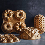 Assorted gold Nordic Ware bundt and loaf pans arranged on a dark surface, including the Jubilee loaf pan at right.
