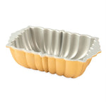 Gold-colored Nordic Ware fluted loaf pan shown from an angle highlighting its scalloped exterior and silver interior finish
