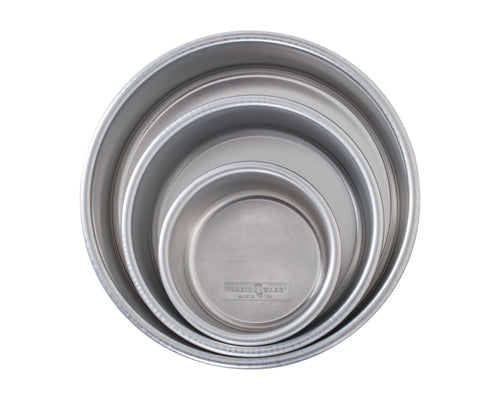 Three nested round aluminum cake pans viewed from above, showing interior rims and brand stamp