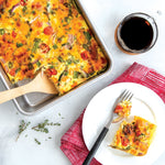 Overhead scene of a baked egg casserole in a Nordic Ware aluminum pan with a plated serving and coffee